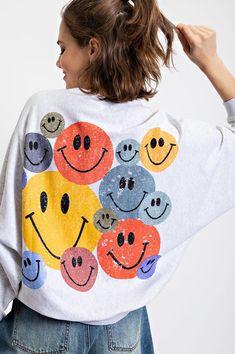 a woman wearing a white sweatshirt with smiley faces on it and her hair in the air