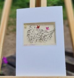 a white frame with some flowers in it on a wooden table next to a purple flower