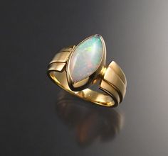 a gold ring with an opal stone in the center on a black surface,