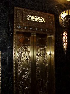 two metal doors in the middle of a wall with lights above them and an ornate design on the door