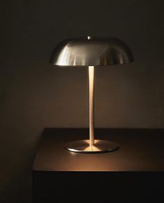 a table lamp sitting on top of a wooden table next to a black wall and floor