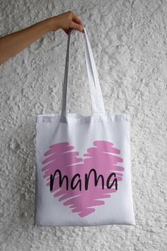 This Mama with a pink heart Tote Bag is a pretty and fun way to carry what you need and go. Buy one to take along with you for your daily needs, or several to get all your shopping done. Great for groceries, shopping, books, gym clothes, or just about anything else. She's sure to get lots of compliments and use it all the time. This listing is for 1  14" x 14" beige, black, or white tote bag with Mama with a pink heart design on 1 side  Nicely packaged in a cellophane bag. Ready to gift Cute White Bag For Valentine's Day, Cute Pink Heart-shaped Bag, Cute White Bags For Valentine's Day, Cute Heart-shaped Pink Bag, Pink Heart-shaped Bag For Valentine's Day, Casual Heart Print Bags For Daily Use, Pink Shoulder Bag For Valentine's Day Gift, Casual White Heart-shaped Bag, Pink Heart-shaped Bag With Heart Print