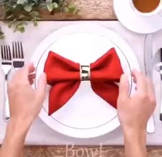 two hands holding forks and knives over a plate with a red bow tie on it