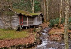 a small cabin in the woods next to a stream