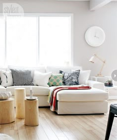 a living room filled with lots of white furniture and pillows on top of wooden flooring