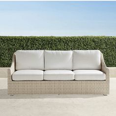 a white couch sitting on top of a cement floor next to a green hedge covered wall