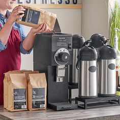 a woman in an apron is making coffee at a counter with two espresso machines