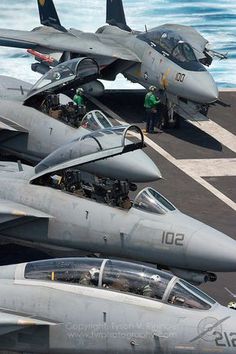 fighter jets lined up on the flight deck of an aircraft carrier, with two men standing next to them