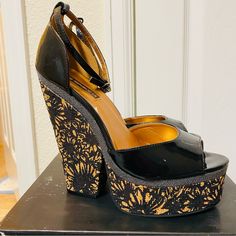 Beautiful Black Patent Wedge On A Cork Wedge With Black Flower Stamp Print And Gold Accents And Ankle Straps. Some Cracking On The Patent Of One Shoe But They Were Never Worn Out. Sky High 6 In. Heel With A 2 In. Platform. These Do Come With The Original Box. Please See Photos For Approximate Measurements. Wedge Sandals With 4-inch Heel For Night Out, Party Wedge Sandals With 4-inch Heel, Black Synthetic Wedge Sandals For Party, Black Platform Wedge Sandals For Evening, Black Sandals With 4-inch Wedge Heel, Wedge Heel Sandals For Night Out, Spring Night Out Wedge Sandals, Black Ankle Strap Wedge Sandals For Party, Black High Heel Wedge Sandals For Night Out