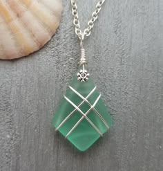 a green glass pendant sitting on top of a silver plate next to a seashell