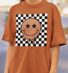 Comfort Colors® Smiley Face Tee Collection: Checkered Smiley Face Crafted from premium 100% ring spun cotton by Comfort Colors, these shirts guarantee comfort and durability. For best results, wash on cold and hang to dry. This Comfort Colors Tee comes in standard unisex sizing. For a more oversized fit, consider sizing up. For those aiming for an oversized "T-shirt Dress" vibe, we recommend going up 2 sizes. Please consult the size chart to ensure the perfect fit for you. If you don't see the color that you want, message us to see if we can make it happen Rest assured, a tracking number will be provided once your order is shipped. Should you encounter any issues or have questions, please don't hesitate to reach out. Your satisfaction is our top priority! Please note: Due to the direct-to- Casual Brown Top With Graphic Design, Brown Cotton Top With Graphic Design, Brown Cotton Graphic Design T-shirt, Brown Graphic Tee With Graphic Design, Brown Cotton T-shirt With Logo Print, Brown Crew Neck Graphic Tee Shirt, Brown Crew Neck Graphic Tee, Brown Cotton Tops With Logo Print, Brown Graphic Tee With Logo Print