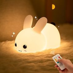 a person holding a remote control in front of a lamp that looks like a rabbit