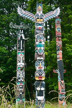 several totem poles in the grass near trees