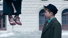 a young boy is standing in front of a building with shoes hanging from his feet