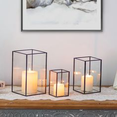 four candles are lit on a table in front of a white wall and framed photograph