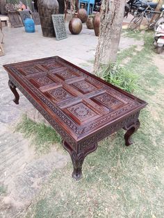 an old wooden table sitting on the ground in front of a tree and potted plant