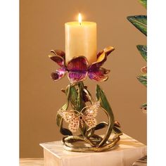 a candle that is sitting on top of a small stand with flowers and butterflies around it