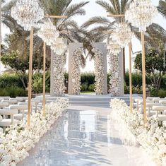 an outdoor wedding setup with white flowers and chandeliers on the aisle, surrounded by palm trees