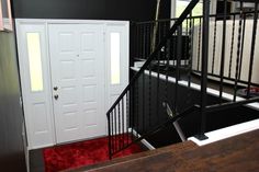 a black and white stair case with red carpet on the floor next to a door