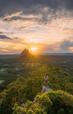 a woman standing on top of a lush green hillside under a cloudy sky at sunset