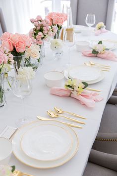 the table is set with pink and white flowers in vases, goldware, and plates