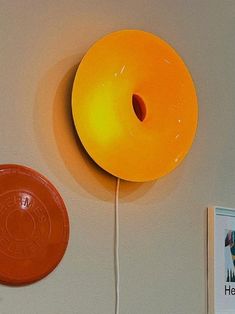 a yellow donut on the wall next to a red frisbee and a book