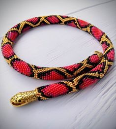 a red, black and gold beaded snake on a white table with wood flooring