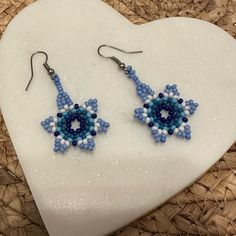 a pair of blue and white beaded earrings sitting on top of a heart shaped rock