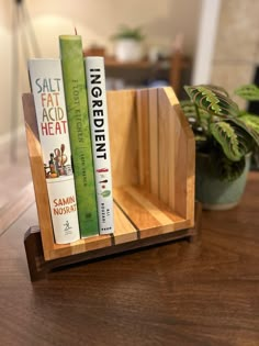 three books are in a wooden holder on a table next to a potted plant