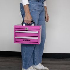 a woman holding a pink toolbox with two drawers on one side and a black handle on the other