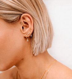 a woman with blonde hair is wearing gold ear cuffs and has two small diamond studs on her left ear