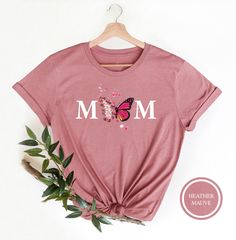 "Mom Butterfly Shirt Hi! Welcome to my store, I'm delighted to see you here. My store's main goal is to provide you with premium everyday apparel with the best graphic t-shirts.  DESCRIPTION * Printed and shipped from the USA. * We use state of art printing on soft and quality shirts. * Different size options; crewneck, youth, women's v-neck, toddler, and baby size options.  * Effective customer service and expedited shipping.  * Solid colors are 100% airlume combed and ringspun cotton.  * Heather colors 52/48 cotton/polyester. * Shoulder taping. Side-seamed. Fitted at bicep. Tear-away label. 4.2 oz. SIZES AND COLORS:  * Please refer to the size charts for measurements before placing an order. * You can compare our numbers to one of your favorite shirts to make sure. * Unisex shirts are tr Mother's Day Pink Graphic Tee, Pink Graphic T-shirt For Mother's Day, Pink Casual T-shirt For Mother's Day, Pink Funny Print T-shirt For Mother's Day, Mother's Day Shirt With Custom Print And Relaxed Fit, Relaxed Fit Shirt With Custom Print For Mother's Day, Funny Print Short Sleeve Shirt For Mother's Day, Mother's Day Crew Neck Cotton Shirt, Mother's Day Cotton Crew Neck Shirt