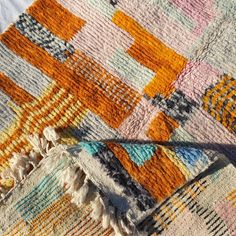 a multicolored blanket laying on top of a bed next to a white pillow