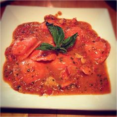 a white plate topped with meat covered in sauce and garnished with green leaves