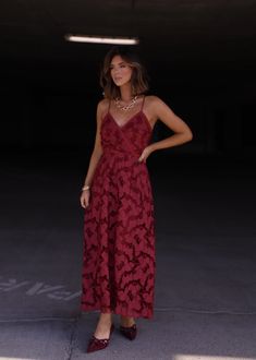 a woman wearing a red dress standing in a parking garage with her hands on her hips