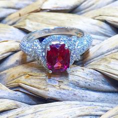 a ring with an oval shaped red stone surrounded by white and blue diamonds on top of dry grass