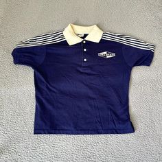 a blue polo shirt with white stripes on the sleeves and collar is laying on a gray carpet