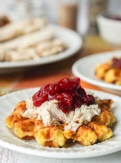 two white plates topped with waffles covered in cranberry sauce and chicken