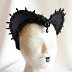 This is a purple and black version of one of most successful designs called Countess. This vampire style headdress is covered with dark purple taffeta and embellished with black cord trimming all around the edges.It is further trimmed with black crystal details that create a halo effect as well as small l beads that were hand-sewn on the trimming to create rich textural interest. The piece is completed with a black crystal handmade element placed at the center front for all that extra drama that Black Fantasy Cat Ears Costume Accessories, Fitted Black Cat Ears Costume Accessories, Black Cat Ears Fantasy Costume Accessories, Halloween Cosplay Costume Accessories With Tall Crown, Fitted Halloween Costume Accessories With Cat Ears, Fitted Cat Ears Halloween Costume Accessories, Fitted Black Headpiece For Evening, Gothic Crown For Party Costume Accessories, Gothic Costume Hats And Headpieces For Masquerade Carnival