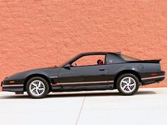 a black sports car parked in front of a pink wall