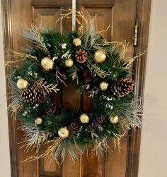 a wreath with pine cones and gold ornaments hangs on the front door to welcome guests