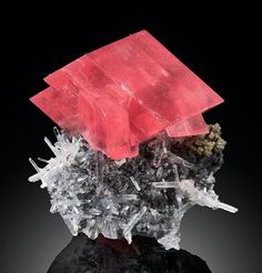 a piece of crystal with red and black crystals on it's surface, against a black background