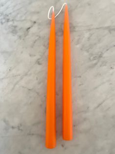 two orange plastic toothbrushes sitting on top of a marble counter next to each other