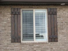 an old brick building with two windows and shutters on each side, one has a black cat sitting in the window