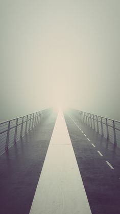 a foggy bridge is shown in black and white with the light at the end