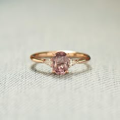 a pink diamond ring sitting on top of a white cloth covered table with a light blue background