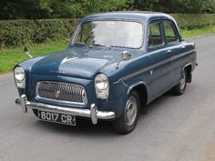 an old blue car is parked on the side of the road in front of some bushes