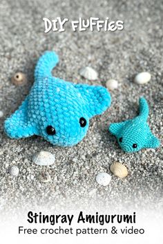 a blue stuffed animal sitting next to a fish on top of a sandy beach with shells