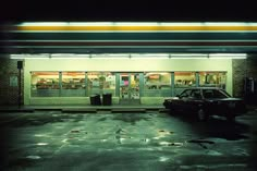 an empty parking lot with a car parked in front of the storefront at night