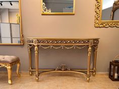 an ornate gold console table in a living room with mirrors on the wall and two stools next to it